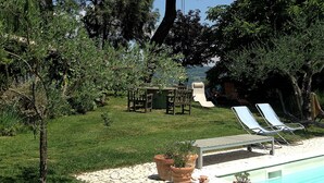 Un área de piscina con sillones de descanso, una mesa y plantas en macetas.