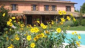 Una casa de dos pisos con techo de tejas, piscina y flores amarillas en primer plano.