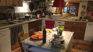 Una cocina con estufa, pileta y diferentes utensilios. Hay una mesa con una botella y un tazón encima.