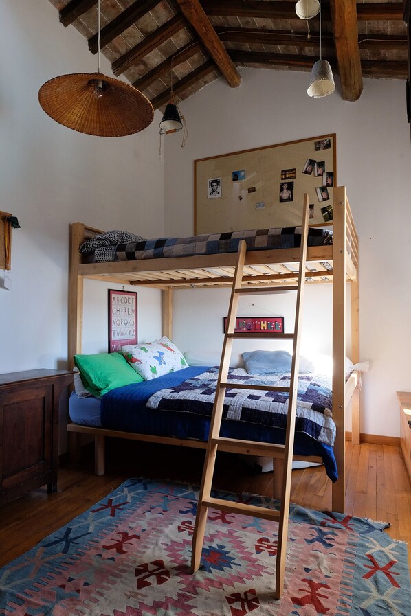 A bunk bed room with a ladder, a wooden desk, a patterned rug, and a wall with photos.