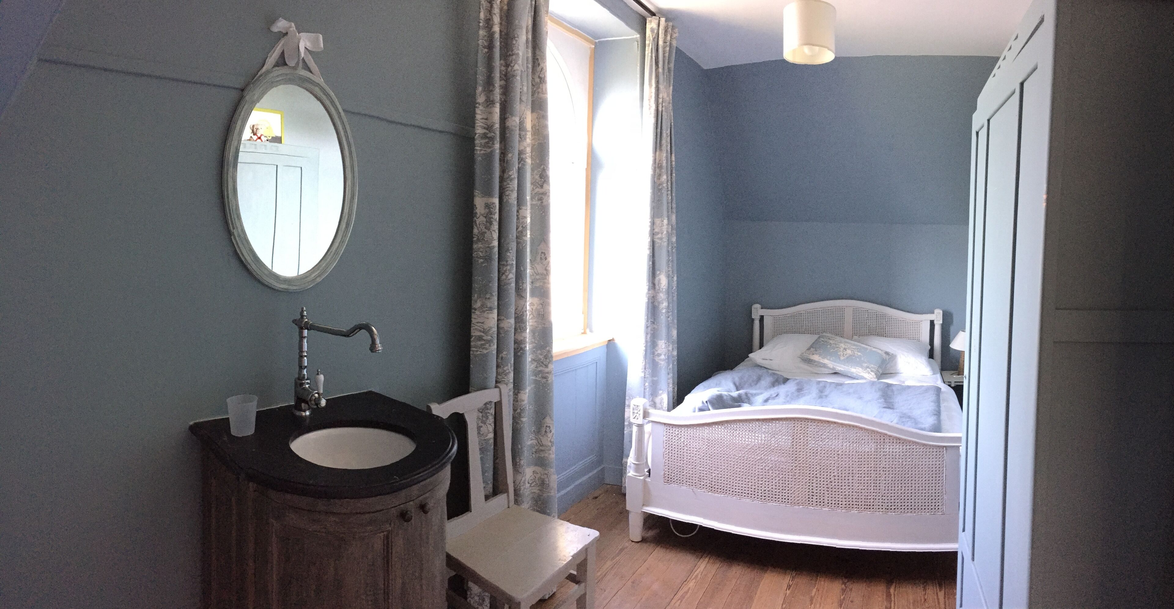 Ein Schlafzimmer mit einem Bett, einem Nachttisch, einem Spiegel und einem Badezimmer mit Waschbecken und einem Sessel.