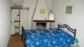 A bedroom with a bed, a wooden headboard, a small table with a lamp, a fireplace, and a ladder against the wall. - Stone house of character in a typical Provencal hamlet (Banon)