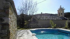 A swimming pool with a stone wall on one side and a building with a bell tower in the background. - Stone house of character in a typical Provencal hamlet (Banon)