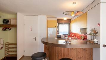 Eine kompakte Küche mit einer Holzbar, einer Mikrowelle und einem Spülbecken. Zwei Hocker und ein kleines Regal mit Küchenutensilien sind vorhanden.