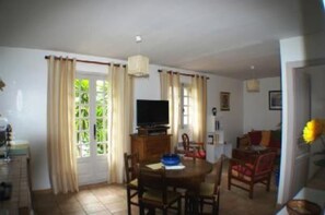 Uma área de refeições com mesa, cadeiras, televisão e cortinas.