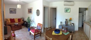 Uma sala de estar com sofá, uma mesa de jantar com cadeiras, uma tigela azul e um vaso com planta.
