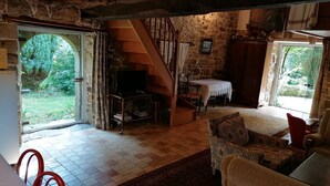A rustic interior with a stone wall, a staircase, a dining area, and a view of greenery outside. - House with character, rustic style House with garden, weekly rental  (Locoal-Mendon)