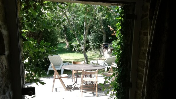 A view through a glass door to an outdoor patio with a table and chairs, surrounded by greenery. - House with character, rustic style House with garden, weekly rental  (Locoal-Mendon)