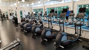 Ein Fitnessstudio mit mehreren Laufbändern und Crosstrainern, großen Fenstern und einem klaren, modernen Design.