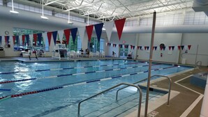 Ein Hallenbad mit mehreren Bahnen, Sicherheitsgeländern und einer Decke mit Industrielampen.