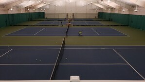 Ein Hallen-Tennisplatz mit mehreren Spielfeldern, Netz und Deckenbeleuchtung.