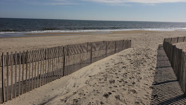 Ein sandiger Strand mit einer Holzlattenzaun und Fußabdrücken, die zum Wasser führen.