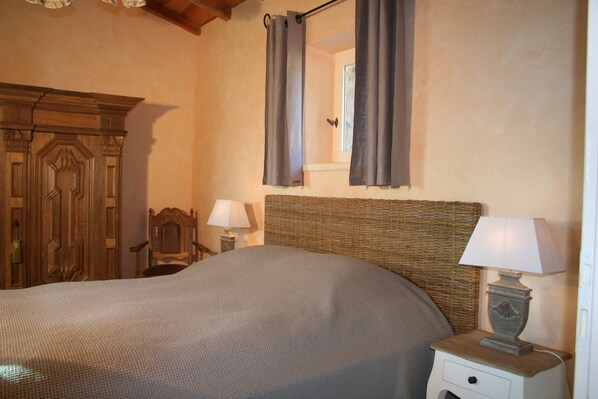 Un dormitorio con una cama grande, un armario de madera, una mesita de noche con una lámpara y una ventana con cortinas.