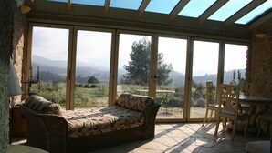 Une pièce dotée d’une grande porte-fenêtre coulissante donnant sur une terrasse, d’un canapé en osier et d’une table à manger avec des chaises.
