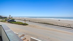 A beachside road with a clear view of the ocean, a parking area, and a pedestrian walkway.