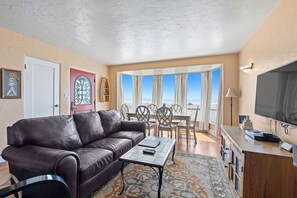A living room with a brown leather sofa, a coffee table, a TV, and a dining area with chairs and a table. - Fabulous Views of the Ocean! (Aptos)