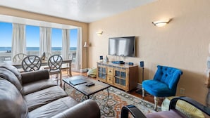 A living room with a sofa, a blue armchair, a television, and a view of the ocean.