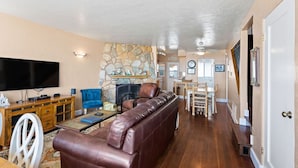 A spacious living room with a stone fireplace, leather sofa, and a flat-screen TV.
