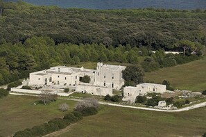 An old stone building with multiple rooms, surrounded by a forested area and a body of water in the background. - Otranto: Apartment/ flat in farm close to Otranto (Otranto)