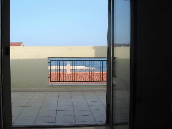 A balcony with a metal railing, a tiled floor, and a view of a building and a body of water.