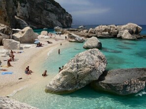 A beach with large rocks, clear turquoise water, and people sunbathing.