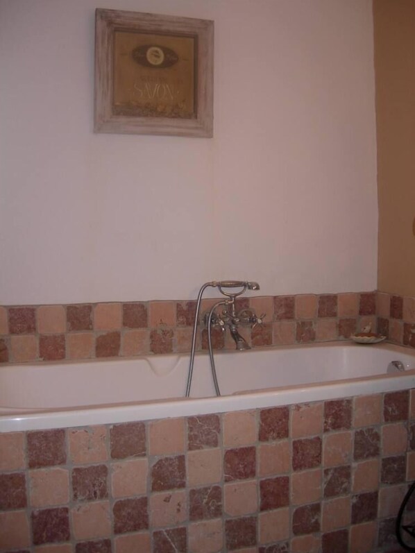 Un baño con bañera, pared de azulejos y un cuadro enmarcado sobre la bañera.