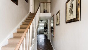 Una escalera con barandilla de madera que lleva a un segundo piso. Un pasillo con piso estampado y obras de arte enmarcadas en las paredes.
