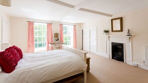 Un dormitorio con una cama grande, un escritorio con silla, una chimenea y una ventana con cortinas.
