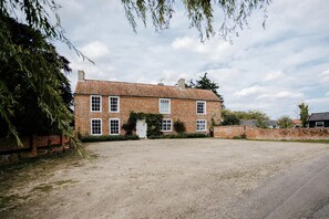 A two-story brick house with a gravel driveway and a brick wall.