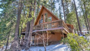 A cabin with a wooden deck and multiple windows, surrounded by tall pine trees and snow. - Yosemite Vista (Yosemite National Park)