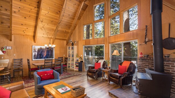 A spacious living area with wooden floors, a fireplace, and large windows offering a view of the outdoors. - Yosemite Vista (Yosemite National Park)