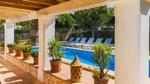 Un espacio al aire libre techado con piscina, sillones de descanso y plantas en macetas.