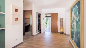 Un pasillo con suelo de madera, una puerta de madera, un cuadro enmarco y una lámpara de pie.