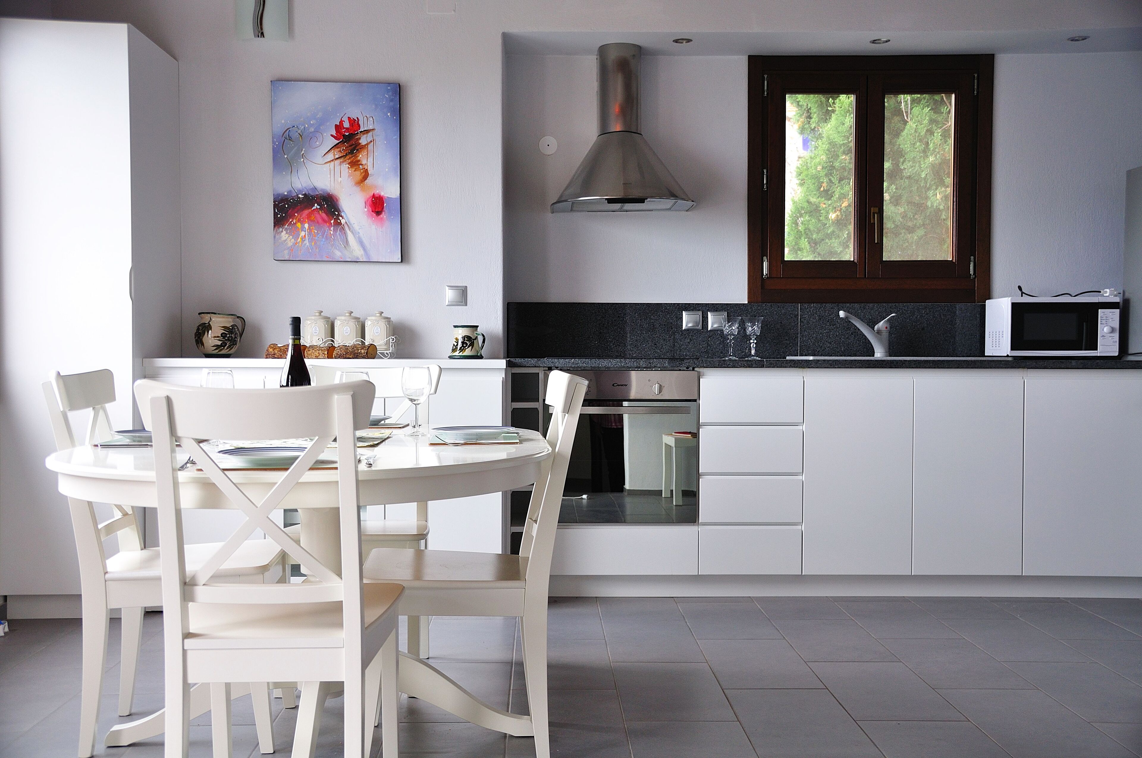 A modern kitchen with white cabinetry, a stainless steel range hood, a microwave, and a dining area with white chairs and a table.