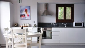 A modern kitchen with white cabinetry, a stainless steel range hood, a microwave, and a dining area with white chairs and a table. - Alonissos, Old Village (Hora) wonderful apartment with amazing  clear sea views (Alonissos)