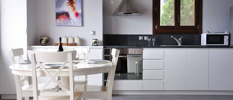 A modern kitchen with white cabinetry, a stainless steel range hood, a microwave, and a dining area with white chairs and a table.
