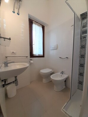 A bathroom with a sink, toilet, bidet, and a window with curtains.