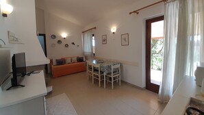A compact living space with a sofa, dining table, and chairs. There are wall-mounted lights and a door with curtains.