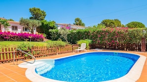 A swimming pool with a wooden deck, surrounded by a wooden fence and a row of pink flowering bushes. - Costabravaforrent Masramon (l'Escala)
