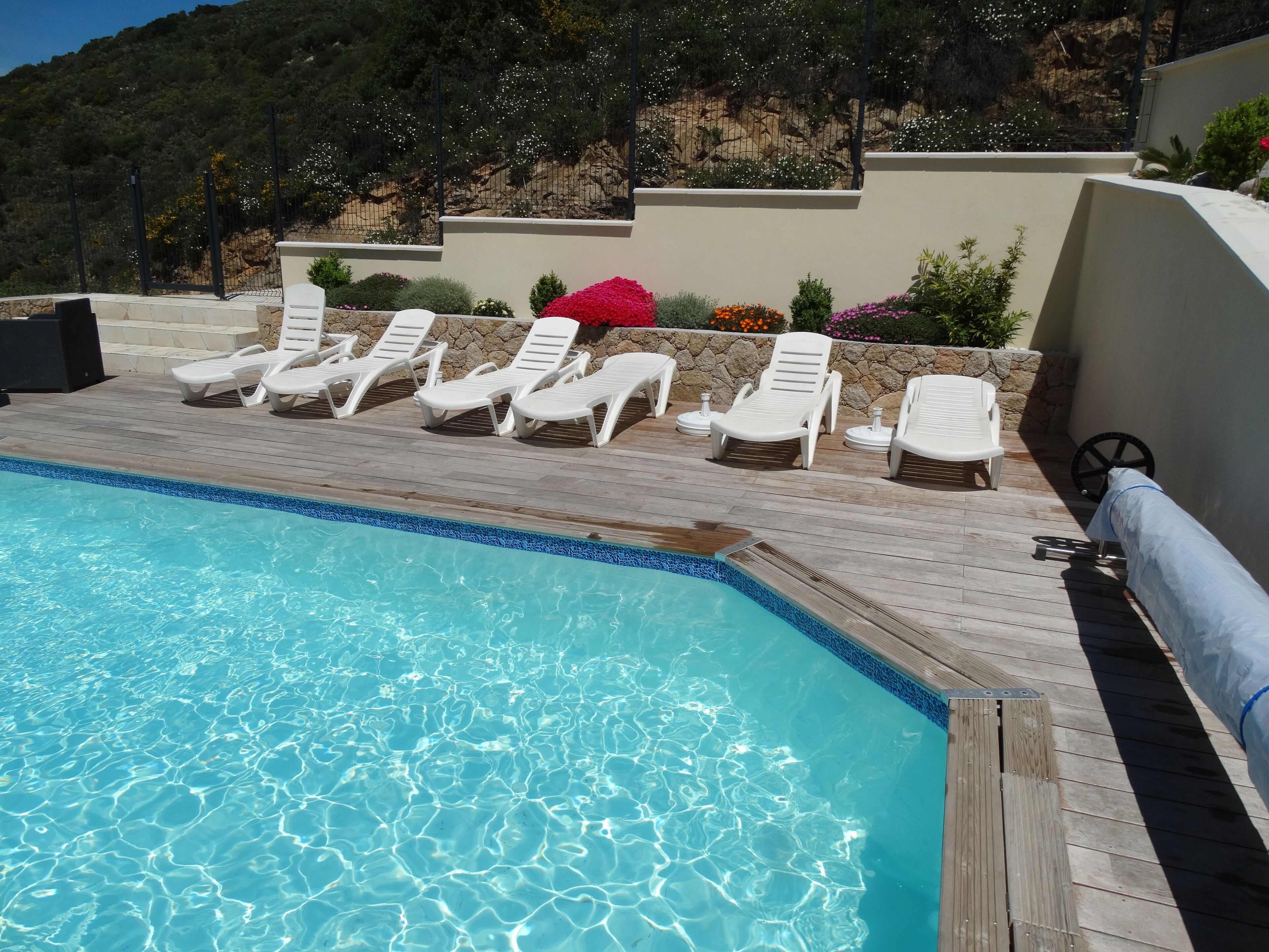 A swimming pool with clear blue water, surrounded by white lounge chairs and a wooden deck.