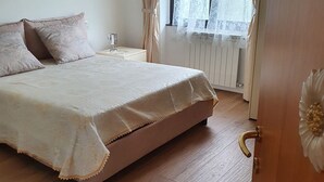 Une chambre à coucher avec un lit, une table de chevet, une fenêtre avec des rideaux et un radiateur.