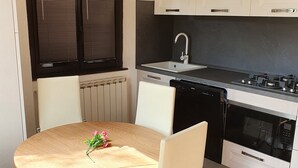 Une cuisine moderne avec des meubles blancs, une cuisinière noire et un four encastré. On y trouve une table à manger avec des chaises et un vase rempli de fleurs.
