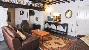 Un salon chaleureux avec un canapé en cuir marron, une table basse en bois et un tapis à motifs. On y trouve un téléviseur posé sur un meuble, une cheminée et un mur décoré de divers objets.