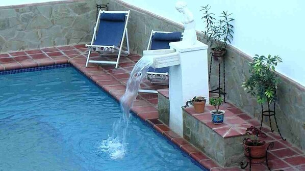 A swimming pool with a waterfall feature, lounge chairs, and potted plants. - Andalucia Center. Beautiful house (ENCINAS REALES)