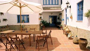 A courtyard with a wooden table and chairs, surrounded by potted plants and a white umbrella. - Andalucia Center. Beautiful house (ENCINAS REALES)
