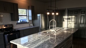 Een moderne keuken met een granieten werkblad, roestvrijstalen apparatuur en een houten kookeiland.
