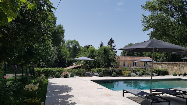 A swimming pool with lounge chairs and umbrellas, surrounded by greenery and a stone building.
