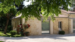 A stone building with a tiled roof, a gravel driveway, and a tree with green leaves.
