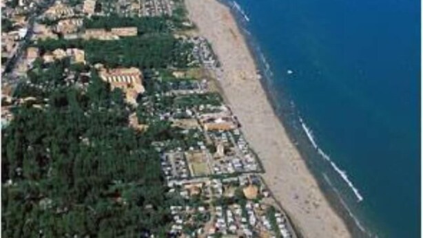 Una vista aerea di una zona costiera con spiaggia, edifici residenziali e un molo che si protende verso il mare.