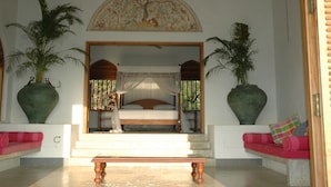 A bedroom with a canopy bed, large potted plants, and a ceiling fan.